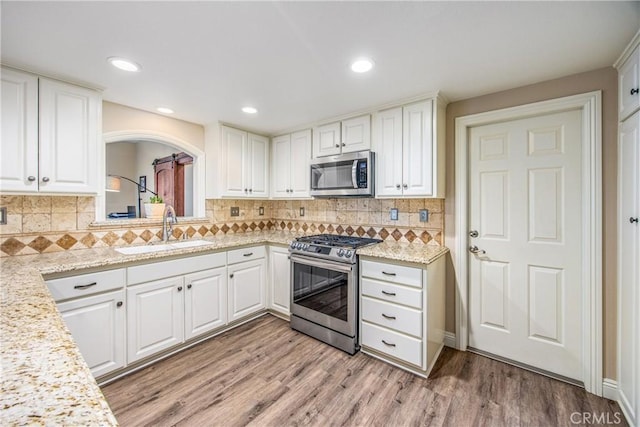 kitchen with light wood-type flooring, appliances with stainless steel finishes, a sink, and white cabinetry