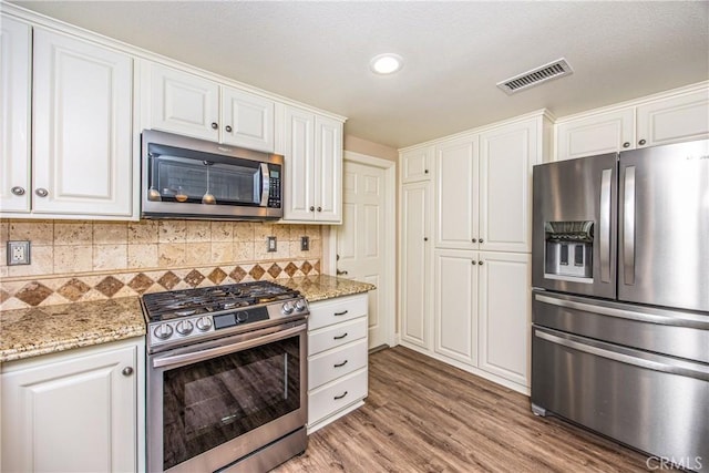 kitchen with tasteful backsplash, light wood-type flooring, white cabinetry, visible vents, and appliances with stainless steel finishes