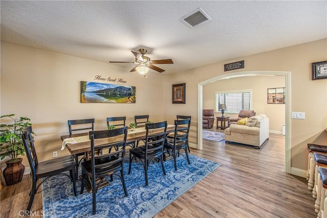 dining room featuring ceiling fan, arched walkways, a textured ceiling, visible vents, and wood finished floors