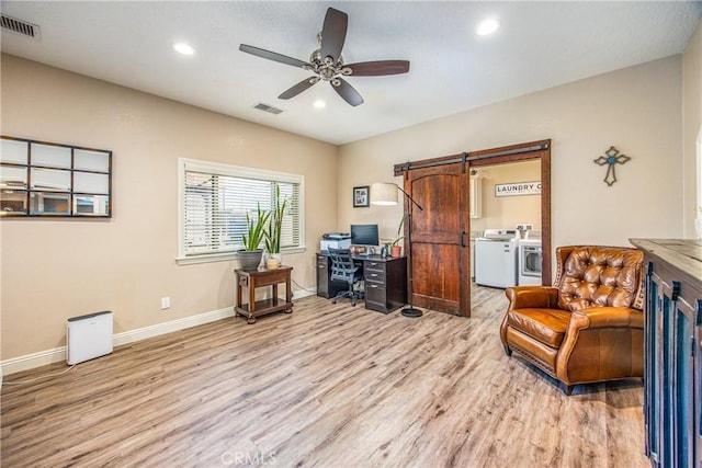 home office featuring visible vents, a barn door, a ceiling fan, light wood finished floors, and washing machine and clothes dryer