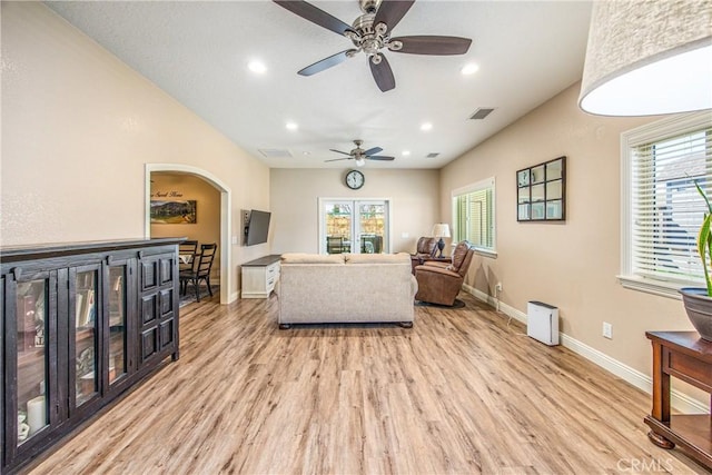living area with ceiling fan, arched walkways, visible vents, light wood finished floors, and baseboards
