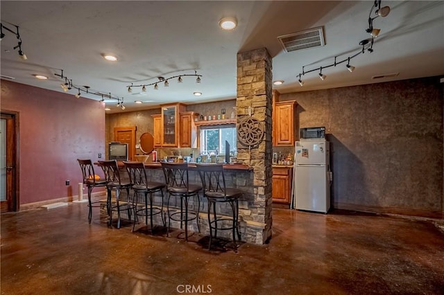 kitchen with brown cabinetry, finished concrete flooring, rail lighting, and freestanding refrigerator