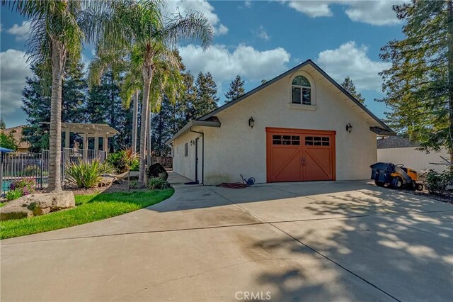 view of front of property with a pergola, a detached garage, concrete driveway, stucco siding, and fence