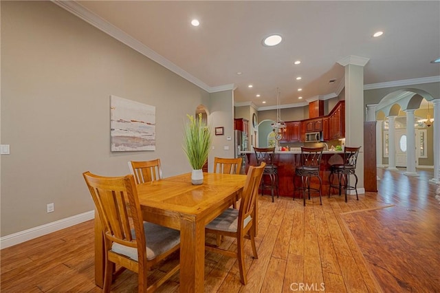 dining area featuring recessed lighting, light wood finished floors, decorative columns, crown molding, and arched walkways