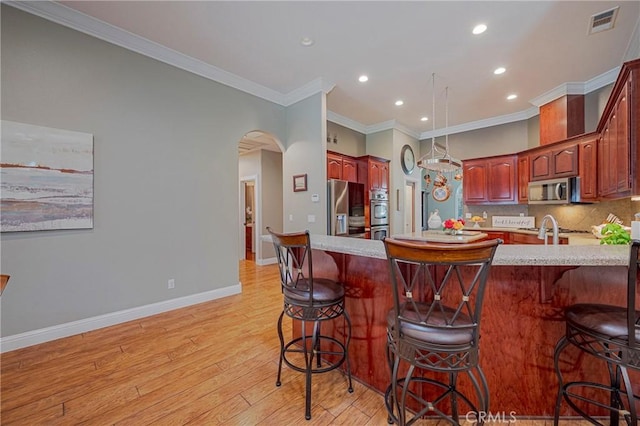 kitchen with recessed lighting, a breakfast bar area, light wood-style floors, appliances with stainless steel finishes, and crown molding