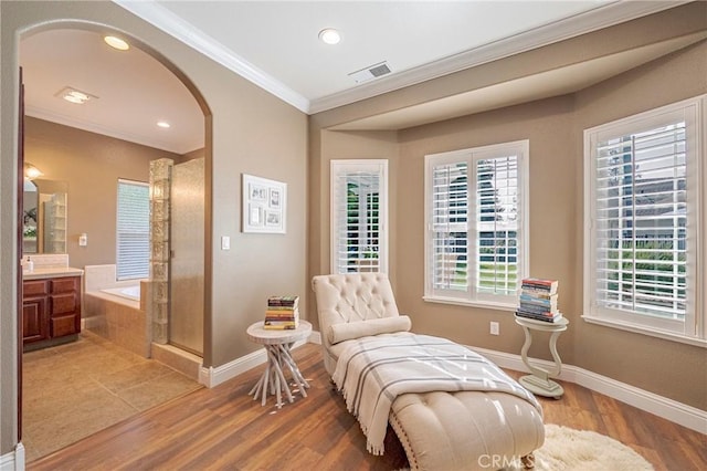 sitting room with crown molding, arched walkways, visible vents, and baseboards