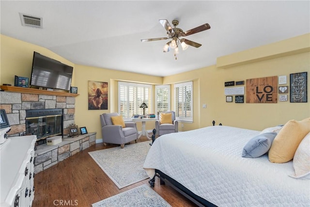 bedroom featuring wood finished floors, a stone fireplace, lofted ceiling, baseboards, and visible vents