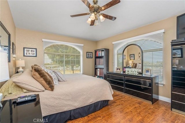 bedroom featuring multiple windows, wood finished floors, baseboards, and a ceiling fan