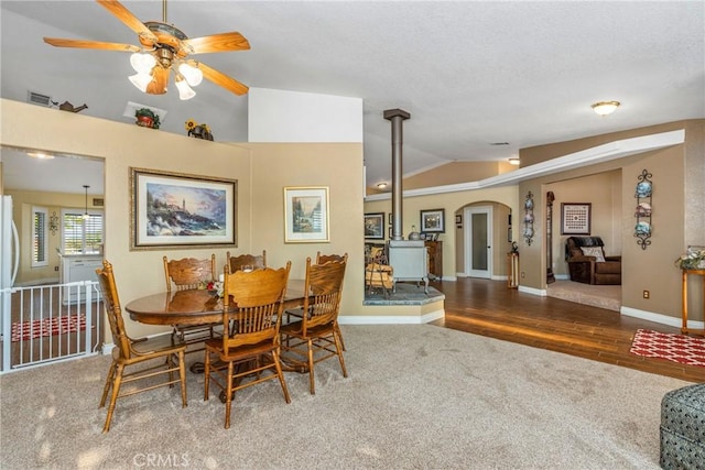 carpeted dining room featuring vaulted ceiling, a wood stove, visible vents, arched walkways, and ceiling fan