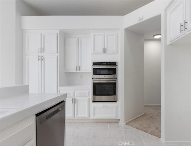 kitchen with light tile patterned floors, white cabinetry, appliances with stainless steel finishes, tile counters, and light colored carpet