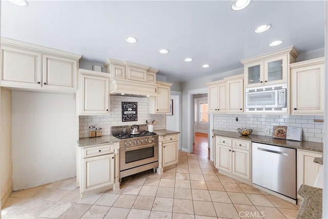 kitchen with cream cabinets, stainless steel appliances, light stone counters, and custom exhaust hood