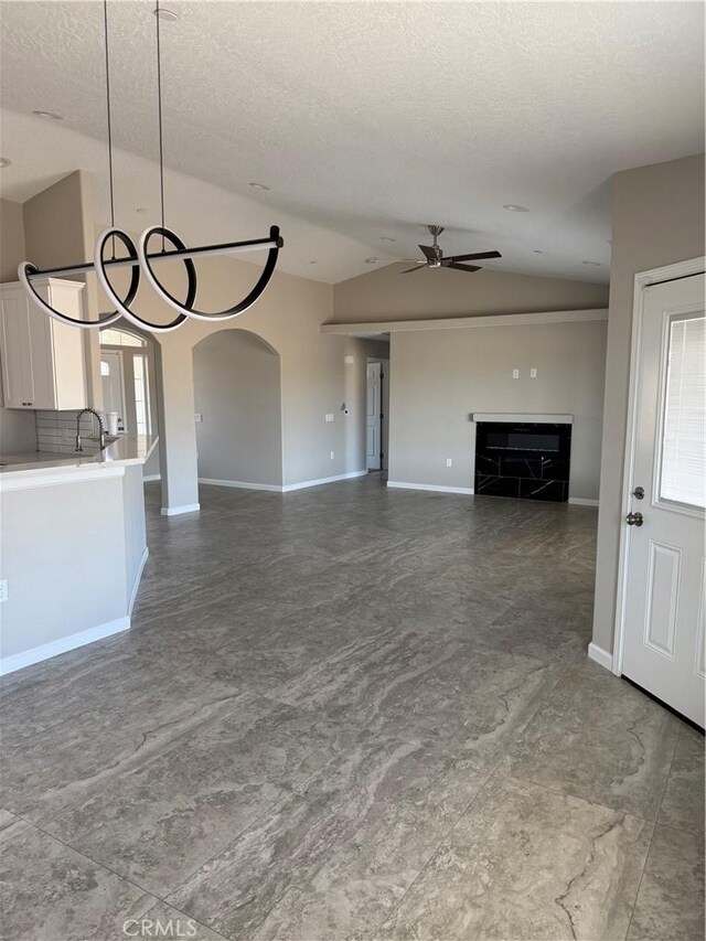 17796 Valencia St, Hesperia, CA 92345 - unfurnished living room with vaulted ceiling, ceiling fan, a fireplace, a textured ceiling, and baseboards