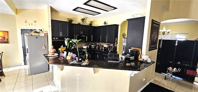 7445 Cedar St, Phelan, CA 92371 - kitchen featuring appliances with stainless steel finishes, arched walkways, dark cabinets, dark stone countertops, and light tile patterned floors