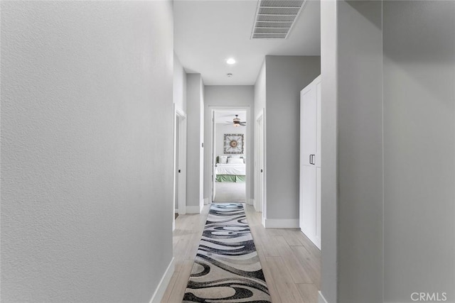 corridor featuring light wood-style floors, visible vents, baseboards, and a textured wall
