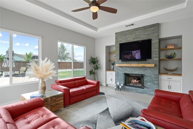 living room with visible vents, built in shelves, a raised ceiling, a ceiling fan, and a fireplace