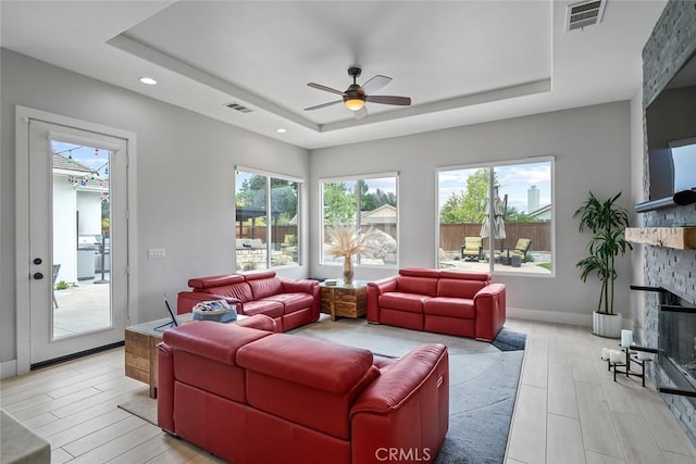 living area with visible vents, a tray ceiling, a ceiling fan, and wood finish floors