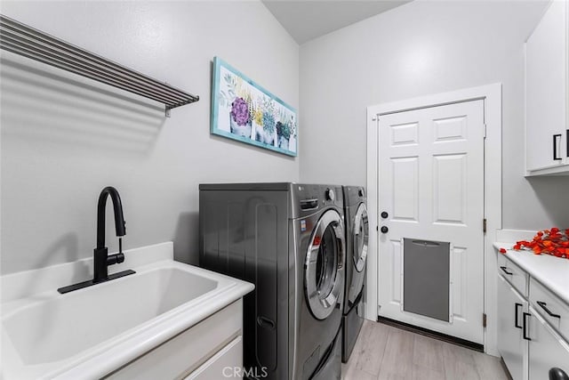 laundry area with light wood-style flooring, a sink, cabinet space, and washing machine and dryer