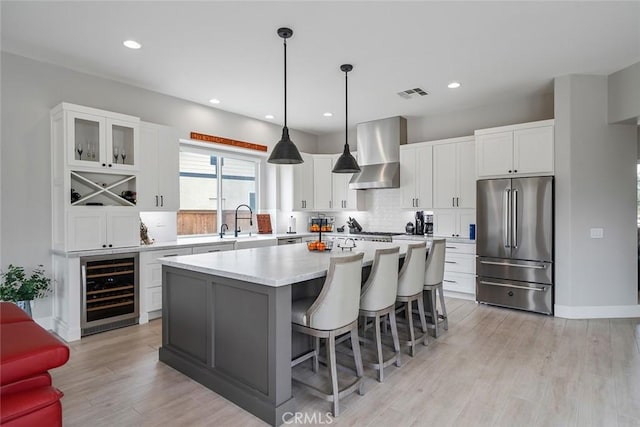 kitchen featuring wall chimney range hood, high quality fridge, visible vents, a center island, and wine cooler