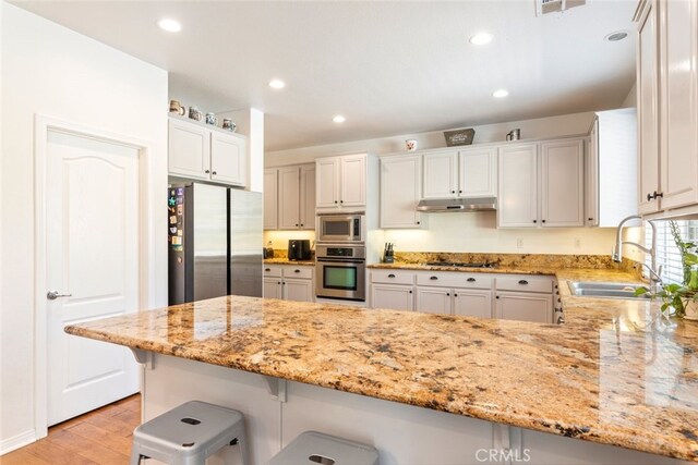 33734 Wild Horse Way, Yucaipa, CA 92399 - kitchen with stainless steel appliances, a sink, under cabinet range hood, a peninsula, and light wood-type flooring