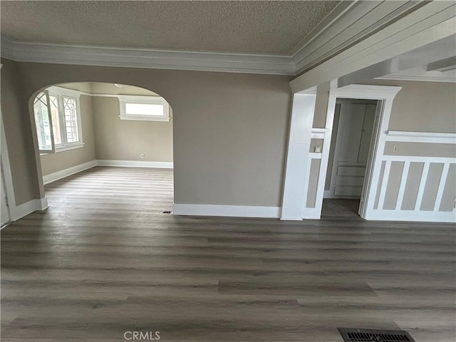 unfurnished room featuring crown molding, wood finished floors, arched walkways, baseboards, and visible vents