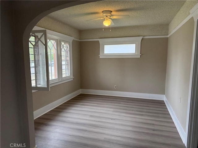 spare room featuring plenty of natural light, wood finished floors, arched walkways, and a textured ceiling