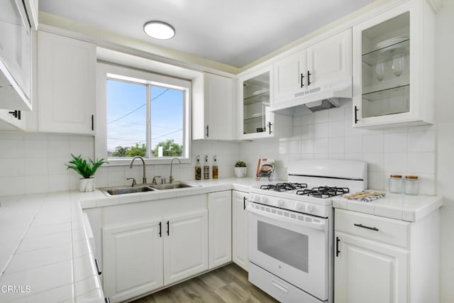 kitchen with tasteful backsplash, white gas stove, white cabinetry, under cabinet range hood, and a sink