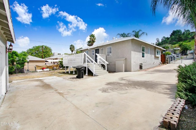 rear view of property featuring a wooden deck, stucco siding, and stairs
