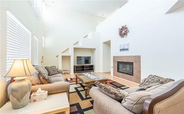 living area featuring a high ceiling, a tiled fireplace, and wood finished floors