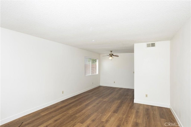 empty room featuring dark wood-style flooring, a textured ceiling, visible vents, baseboards, and ceiling fan
