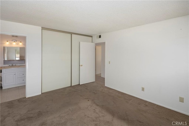 unfurnished bedroom featuring light colored carpet, a textured ceiling, a sink, connected bathroom, and a closet
