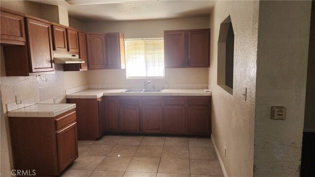 242 E 92nd St, Los Angeles, CA 90003 - kitchen featuring a sink, under cabinet range hood, a textured wall, tile counters, and light tile patterned floors