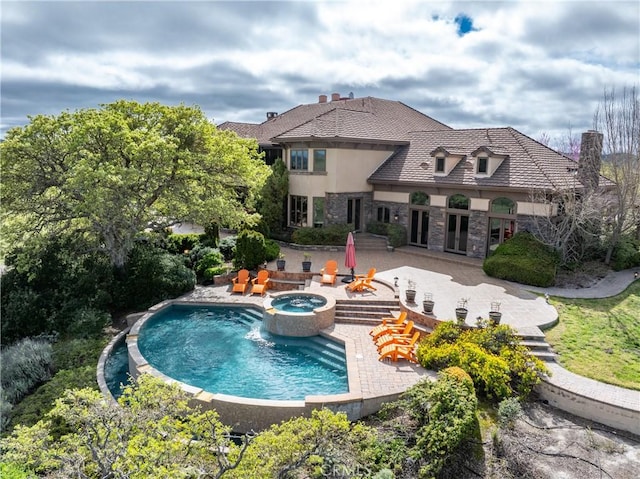 rear view of property featuring stone siding, a pool with connected hot tub, stucco siding, a fire pit, and a patio area