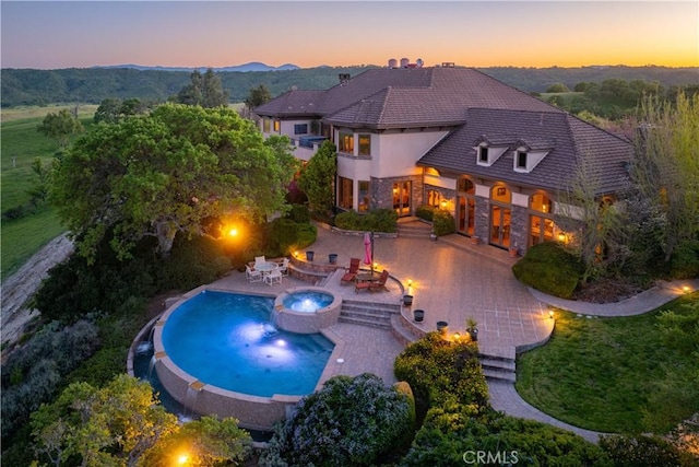 pool at dusk featuring a patio, a fire pit, and a pool with connected hot tub