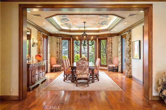 unfurnished dining area with hardwood / wood-style floors, visible vents, an inviting chandelier, and a raised ceiling