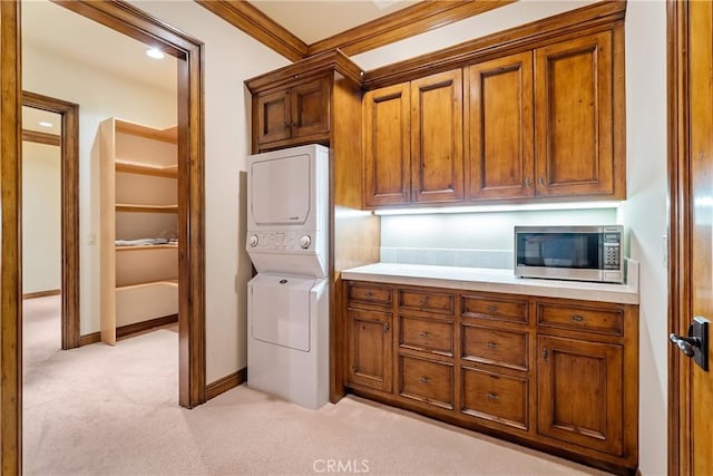 laundry area featuring crown molding, baseboards, light carpet, stacked washer and dryer, and cabinet space