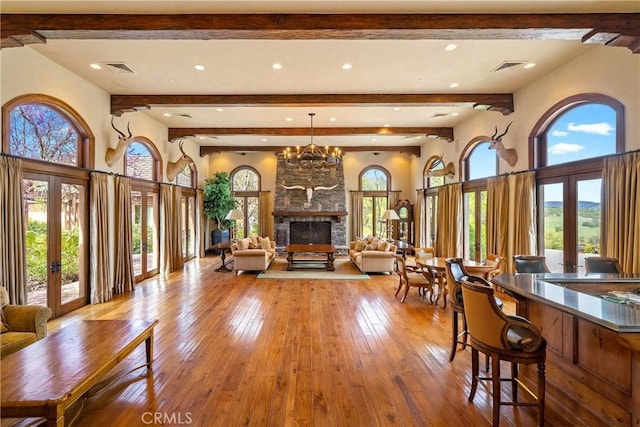 living area featuring hardwood / wood-style floors, beam ceiling, french doors, and a stone fireplace