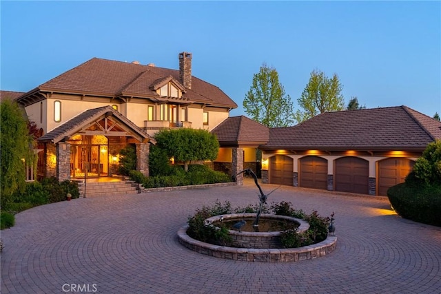 view of front of house featuring stone siding, curved driveway, stucco siding, and a chimney