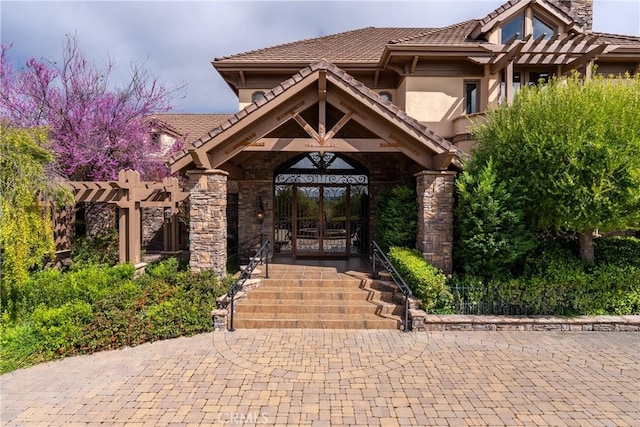 exterior space with stucco siding, a tile roof, stone siding, and a pergola
