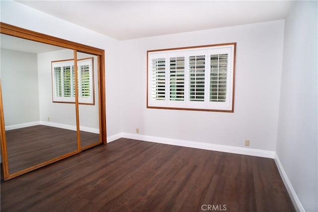 unfurnished bedroom featuring dark wood-style flooring, baseboards, and a closet