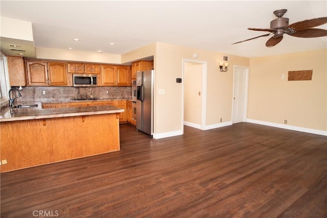 kitchen featuring a peninsula, baseboards, brown cabinets, a sink, and appliances with stainless steel finishes