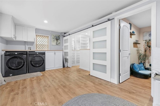 clothes washing area featuring cabinet space, light wood-style flooring, independent washer and dryer, and a barn door
