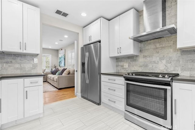 kitchen featuring wall chimney range hood, white cabinetry, dark countertops, and appliances with stainless steel finishes