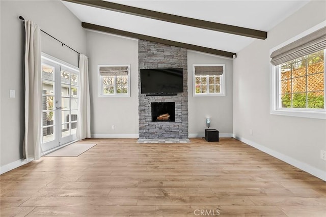 unfurnished living room featuring lofted ceiling with beams, a fireplace, light wood-type flooring, and plenty of natural light
