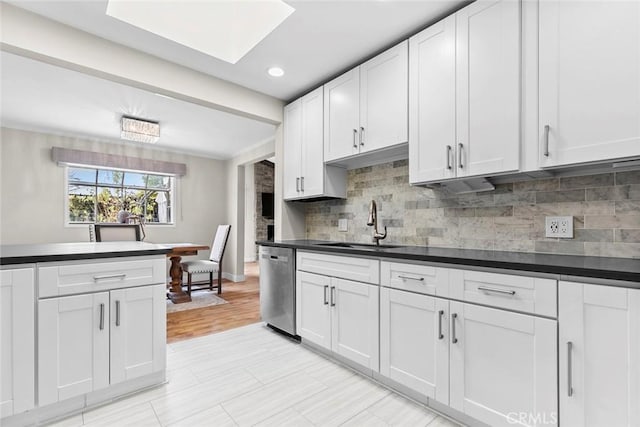 kitchen featuring stainless steel dishwasher, dark countertops, backsplash, and a sink