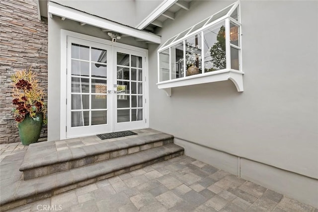 property entrance featuring stucco siding, stone siding, and french doors