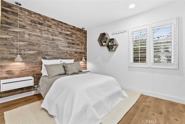 bedroom with an accent wall, wood finished floors, wood walls, baseboards, and recessed lighting