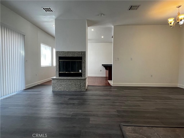 unfurnished living room featuring dark wood-type flooring, baseboards, visible vents, and a notable chandelier