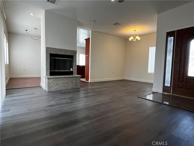 unfurnished living room with baseboards, dark wood-style flooring, a glass covered fireplace, and a chandelier
