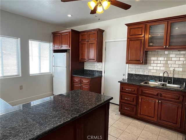 kitchen featuring a sink, freestanding refrigerator, tasteful backsplash, glass insert cabinets, and ceiling fan