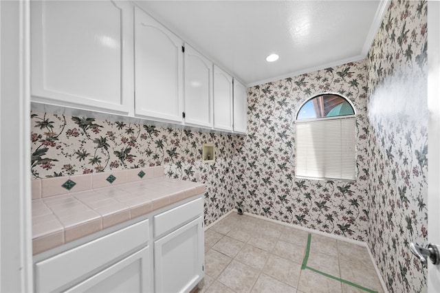 washroom featuring baseboards, wallpapered walls, and cabinet space